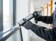 Ein Handwerker führt professionelle Glasreparaturen durch, indem er Dichtmasse an den Fensterrahmen aufträgt.